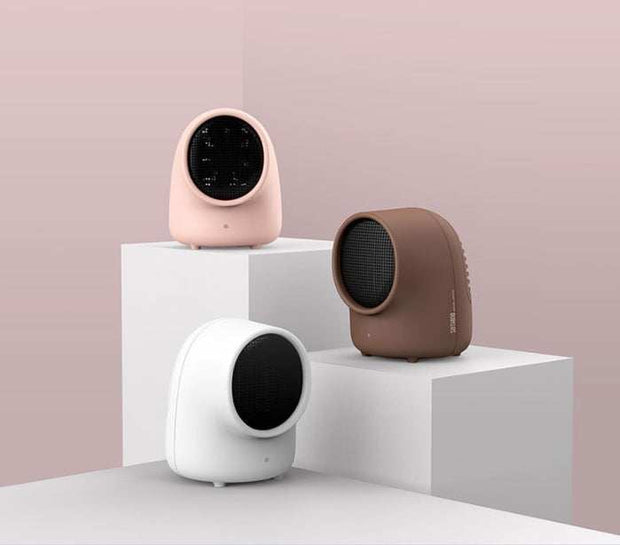 Three compact mini home heaters in pink, brown, and white colors displayed on white geometric platforms against a light pink background.