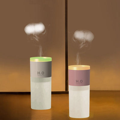 Two compact Home Multi-Mode Diffusers in gray and pink emitting mist on a wooden surface