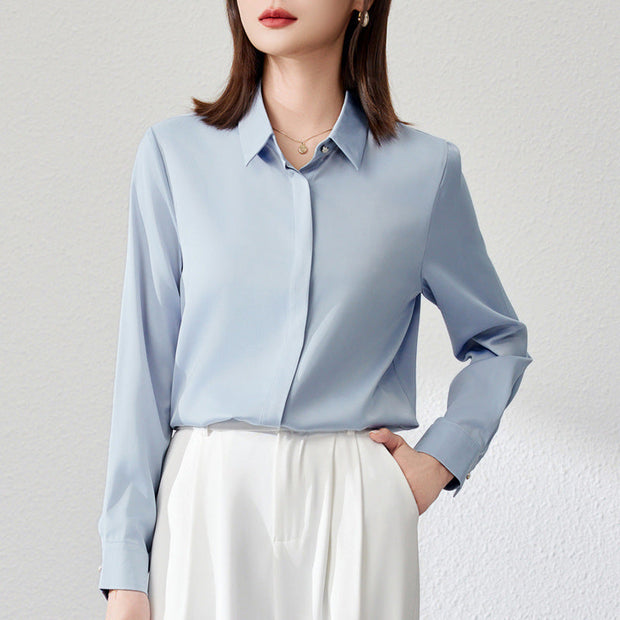 Graceful satin top in light blue with long shirt sleeves and button details, styled in urban fashion.
